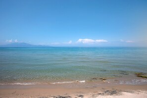 A beach with clear water, a sandy shore, and distant mountains.