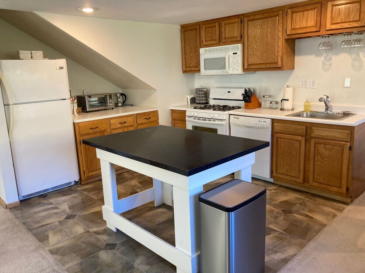 A kitchen with a central island, wooden cabinets, a microwave, stove, and a refrigerator.