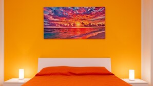A room with a bed, two bedside lamps, and a sunset painting on the wall.
