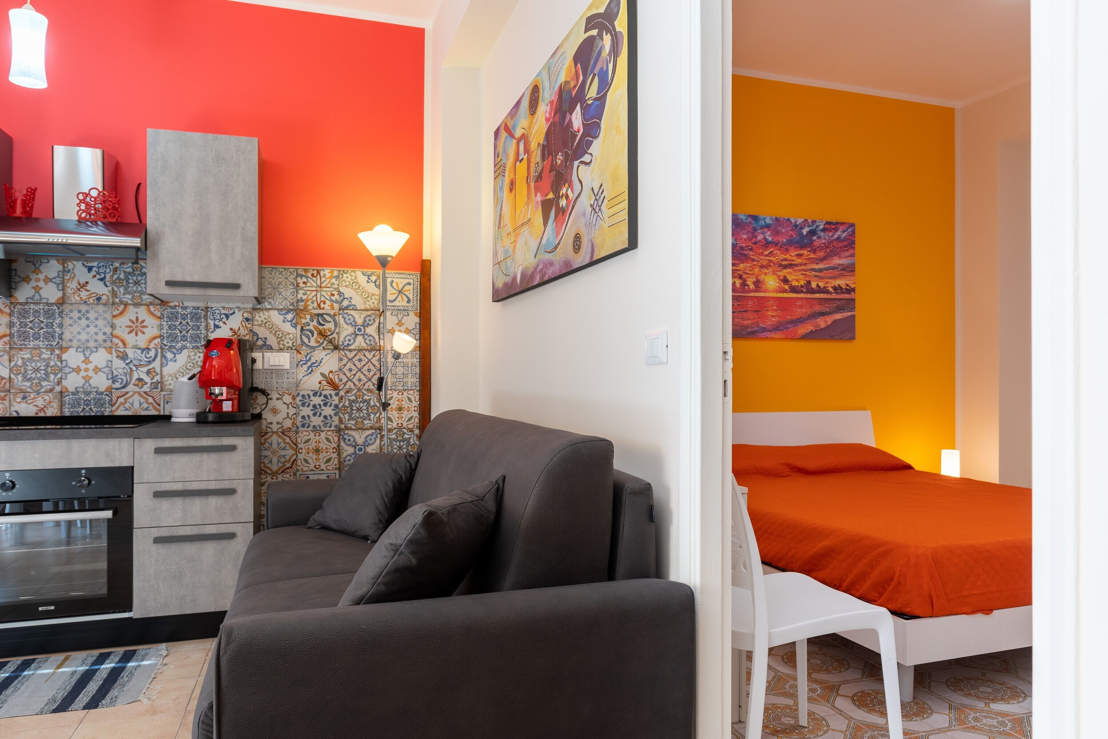 Eine moderne Küche mit Einbauofen, ein graues Sofa und ein Bett mit orangefarbener Bettdecke.