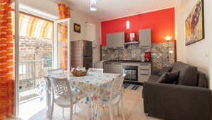 A kitchen with a red wall, a dining area with a table and chairs, and a sofa.