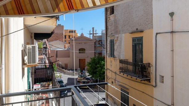 A view from a balcony overlooking a street with buildings, a clear sky, and a parked car.