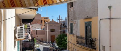 A view from a balcony overlooking a street with buildings, a clear sky, and a parked car.
