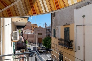 Une vue depuis un balcon donnant sur une rue bordée d’immeubles, avec un ciel dégagé et une voiture garée.
