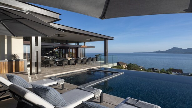 Zona de piscina moderna al aire libre con sillones de descanso y un bar con vistas al mar.