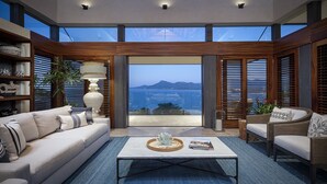 Una sala de estar moderna con un amplio ventanal que ofrece vistas a un cuerpo de agua y montañas.