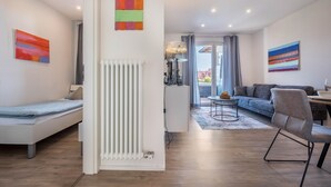 Ein modernes Wohnzimmer mit einer Couch, einem Esstisch und einem Sessel. Ein Heizkörper und eine Lampe stehen auf einem Tisch.