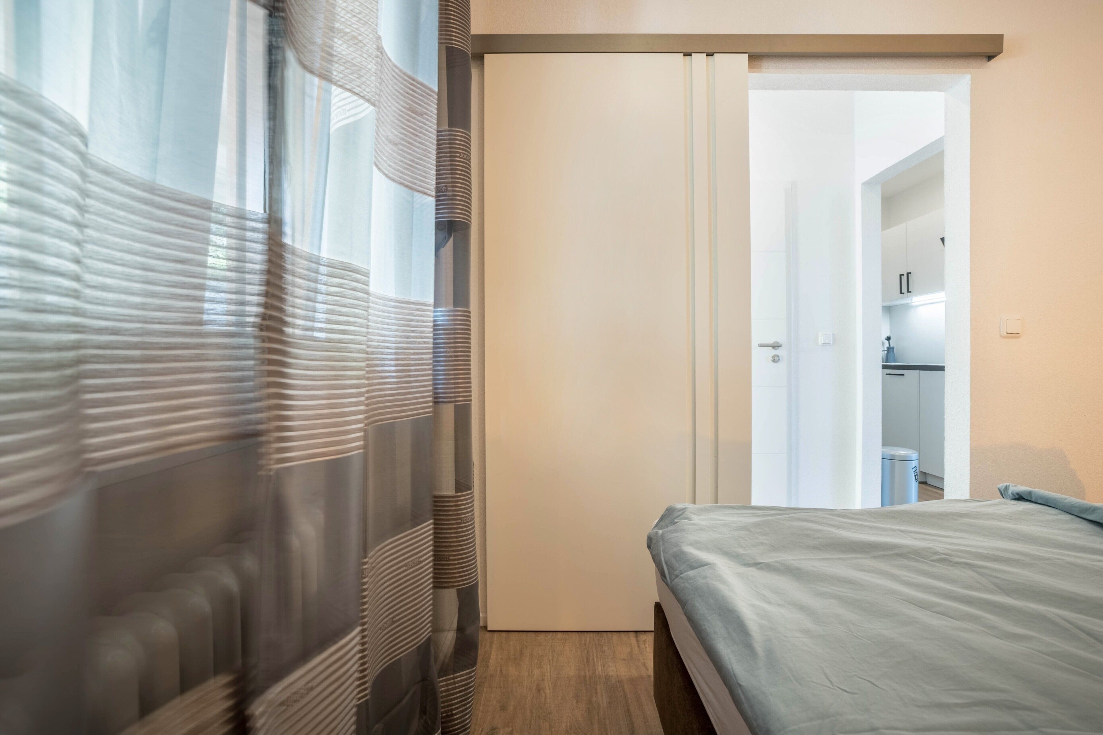 Ein Schlafzimmer mit Bett, einer Schiebetür und Blick in einen Küchenbereich.