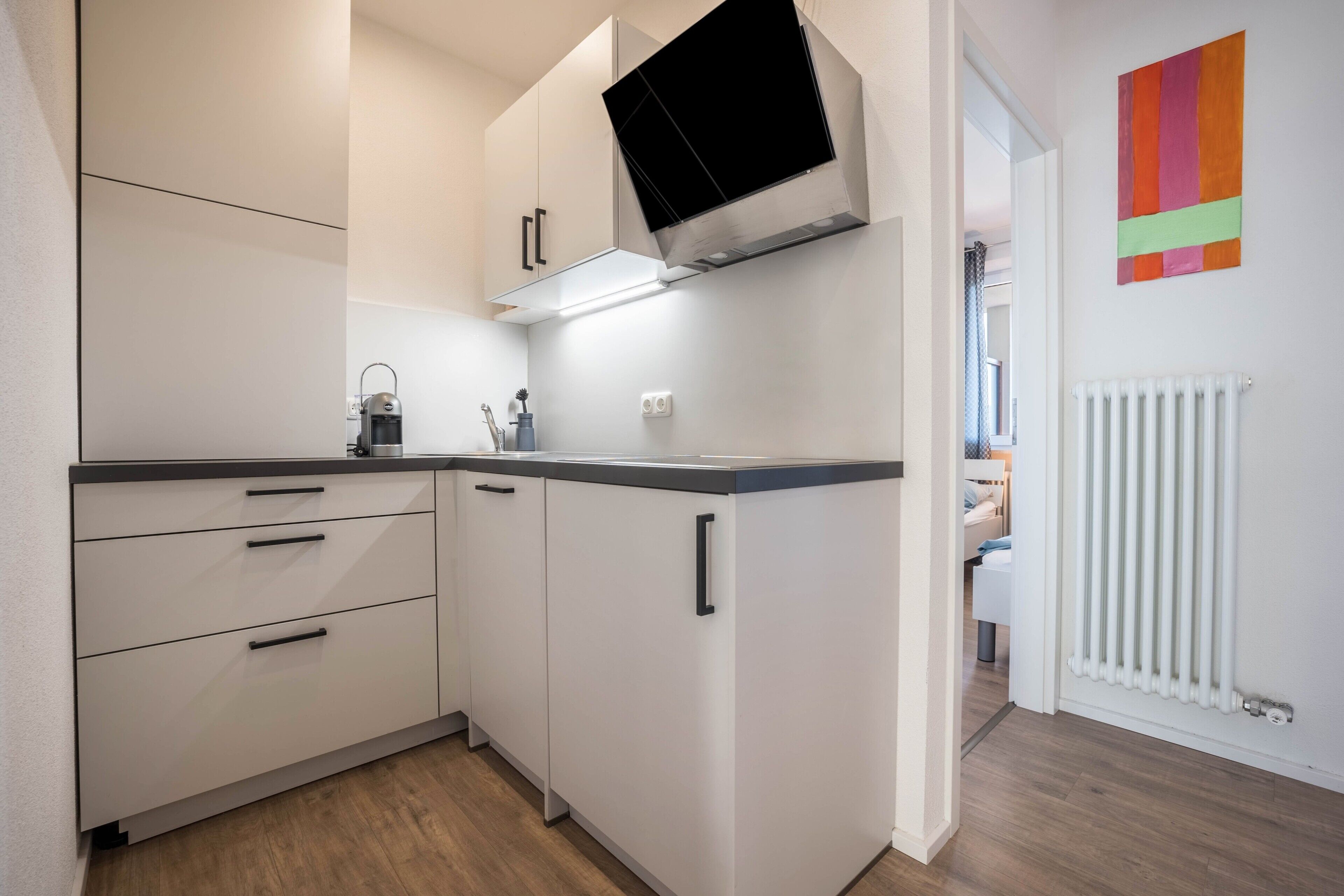 A compact kitchen with white cabinets, a built-in microwave, and a black TV mounted above.