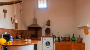 A kitchen with a washing machine, wooden cabinets, a hanging basket, and a window.