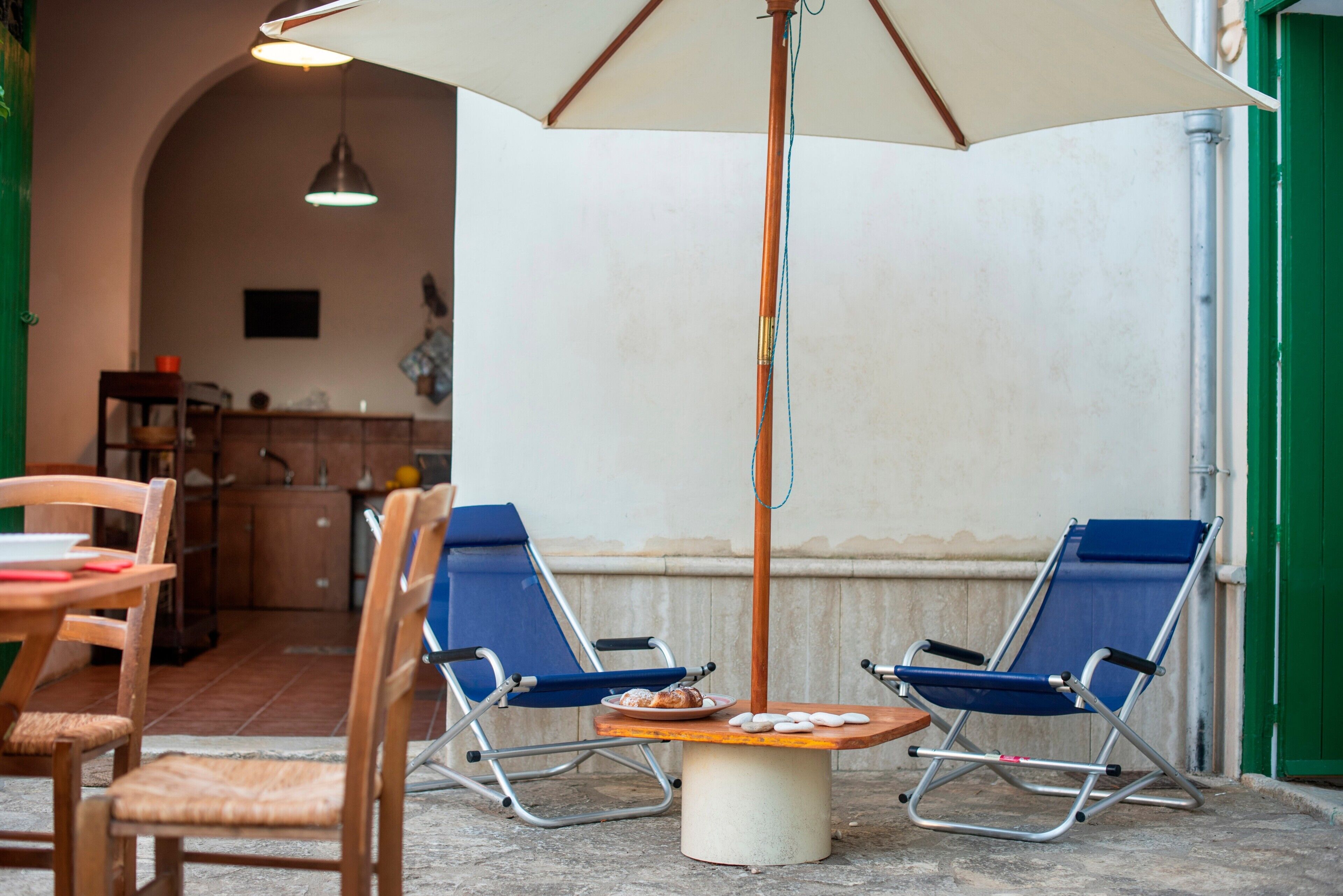 A patio with two blue lounge chairs, a table with a plate of food, and a large umbrella.