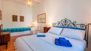 A bedroom with a bed, bedside tables, a desk, a chair, and artwork on the walls.