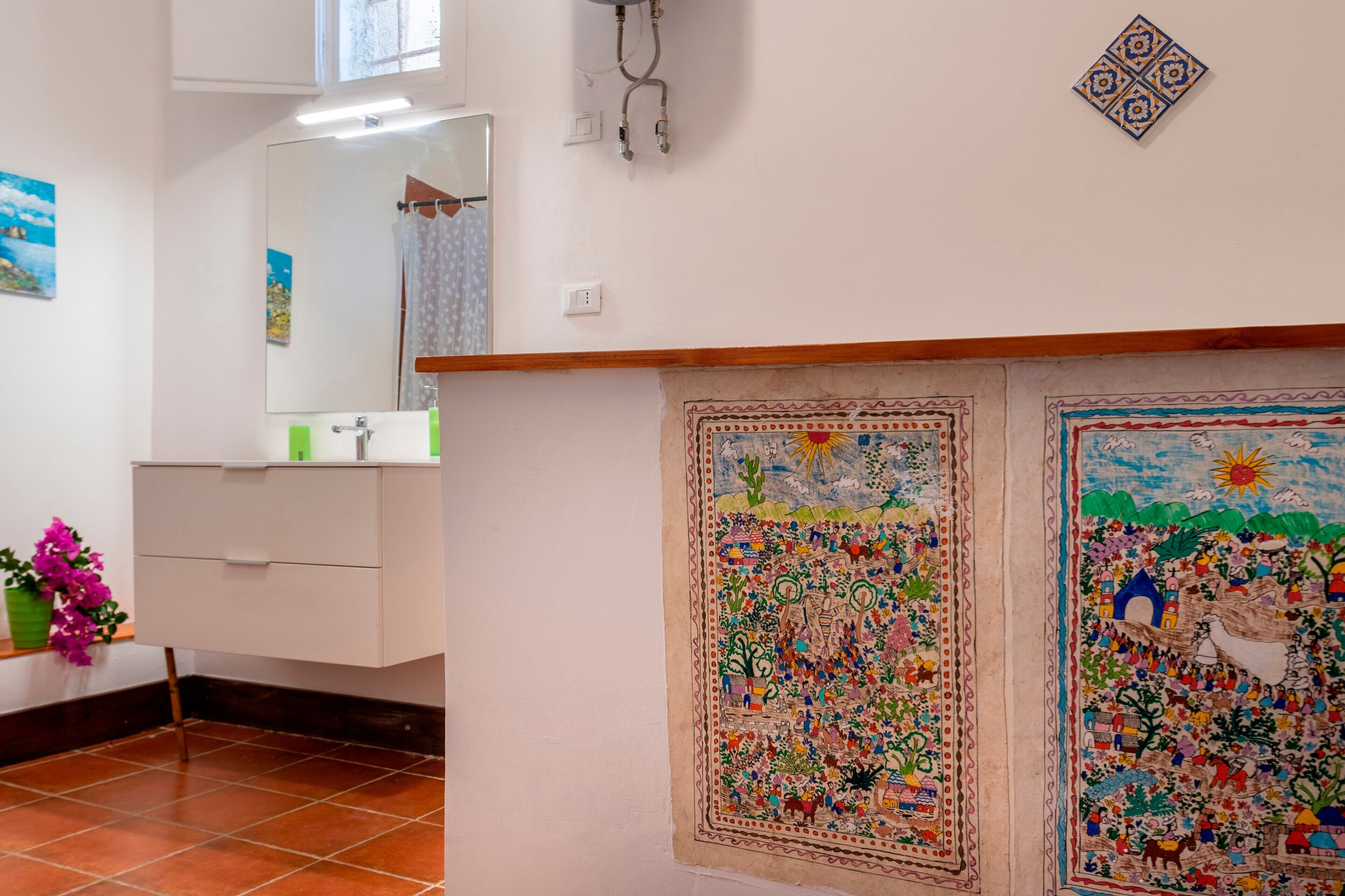 A bathroom with a mirror, a sink, a toilet, and a decorative wall with two colorful murals.