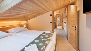A bedroom with a wooden ceiling, a bed with white linens, a green floral blanket, and a wooden door.