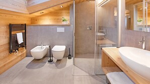 A modern bathroom with a wooden ceiling, a glass shower enclosure, a large sink, and a bidet.