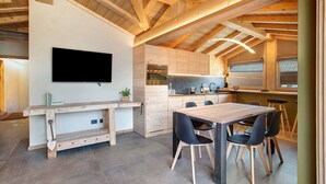 Una cocina moderna con vigas de madera, horno empotrado y comedor con mesa y sillas de madera.