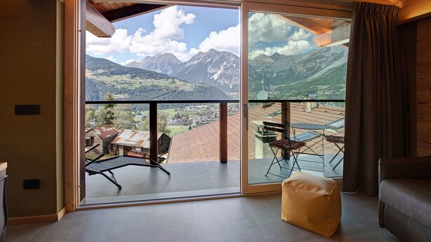 Una habitación con un amplio ventanal corredera que da a un balcón con vistas a la montaña.