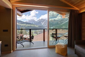 Una habitación con un amplio ventanal corredera que da a un balcón con vistas a la montaña.