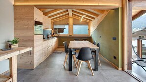 Una cocina moderna con armarios de madera, una zona de comedor con mesa y sillas, y vistas a través de un ventanal grande.