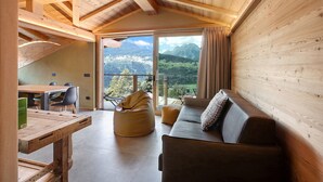 Un interior de madera con comedor, sofá y un amplio ventanal con vista a la montaña.