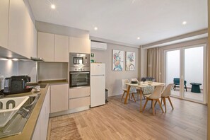 A modern kitchen with a microwave, oven, and refrigerator, a dining area with a table and chairs, and a large sliding glass door leading to a balcony.