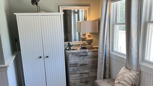 A room with a wooden bench, a white wardrobe, a dresser, and a window with curtains.