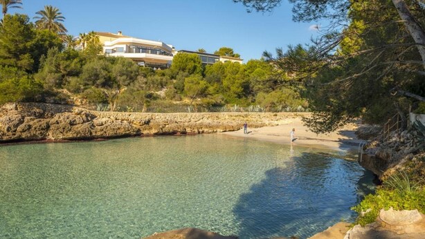 A coastal area with clear water, rocky shore, and a building in the background. - Villa 'Sa Caleta de Cala D'Or' with Sea View, Pool, 2 Terraces & Wi-Fi (Santanyí)