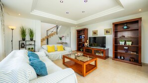 A living room with a sofa, coffee table, TV stand, bookshelf, and staircase. - Villa 'Sa Caleta de Cala D'Or' with Sea View, Pool, 2 Terraces & Wi-Fi (Santanyí)