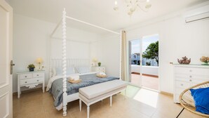 A bedroom with a four-poster bed, a bench, a wicker chair, a nightstand with a lamp, and a dresser. - Villa 'Sa Caleta de Cala D'Or' with Sea View, Pool, 2 Terraces & Wi-Fi (Santanyí)