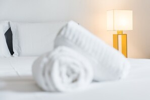 A neatly made bed with a rolled white towel and a bedside lamp. - GuestReady - Modern Duplex, Neo-Classical Building (Porto)
