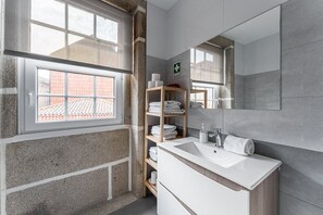 A modern bathroom with a large window, a sink, a mirror, and a shelf with towels. - GuestReady - Modern Duplex, Neo-Classical Building (Porto)