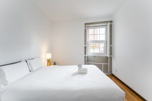 A neatly made bed with white linens, a bedside lamp, and a towel on the bed. - GuestReady - Modern Duplex, Neo-Classical Building (Porto)