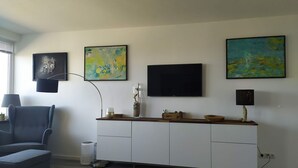 A modern living room with a grey sofa, a white cabinet, and three abstract paintings on the wall. - House Brandenburg App. 43 with lake view - 2 room apartment with breathtaking views (Sylt)