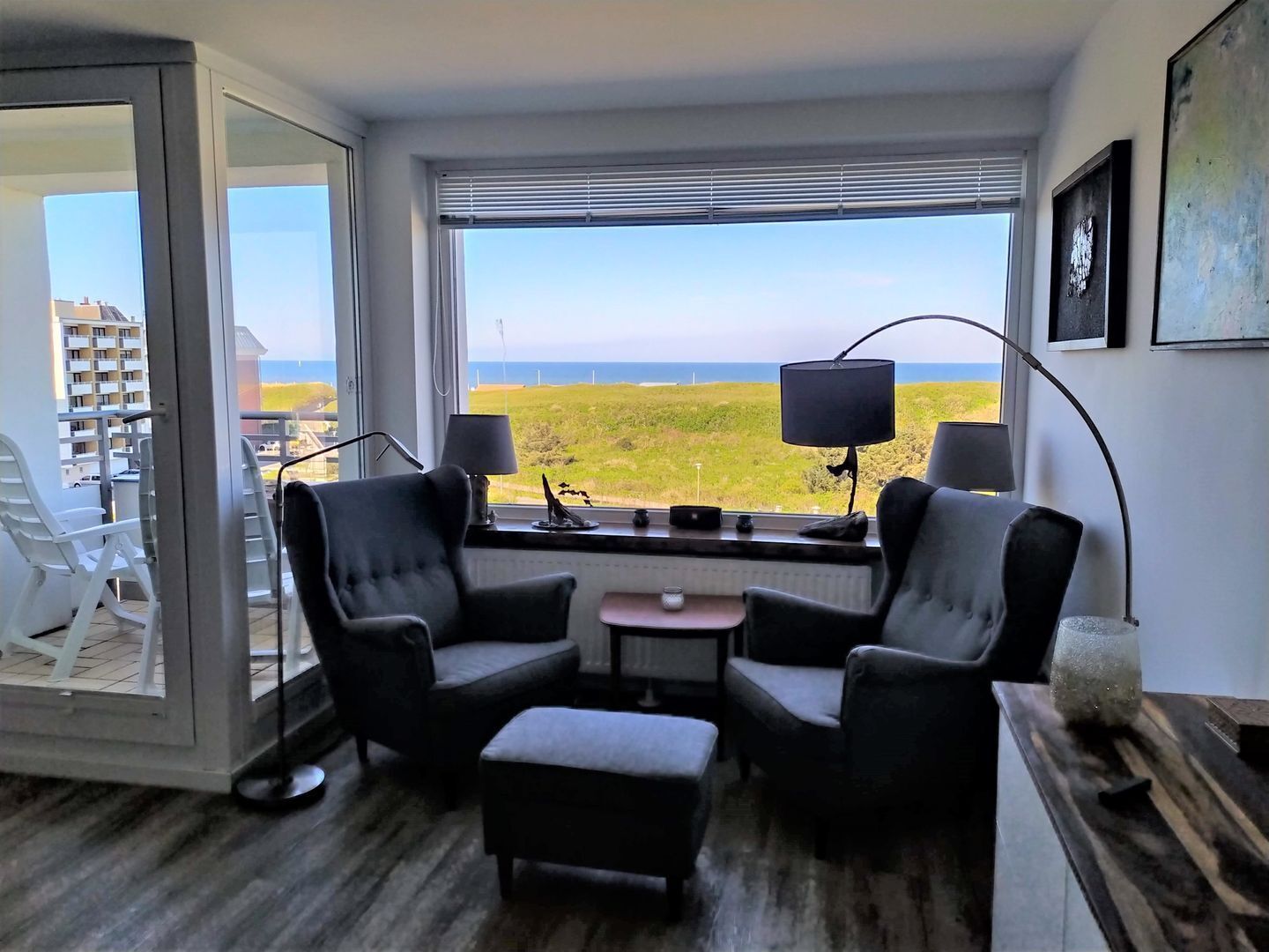 A room with a view of the sea, two armchairs, a small table, and a lamp.