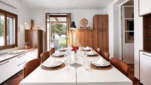 A dining area with a white table set for four, wooden cabinets, and a view of the outdoors. - Villa la Luna – 5-Bedroom Country Estate with Pool & Garden in Vejer, Cádiz (VEJER DE LA FRONTERA)