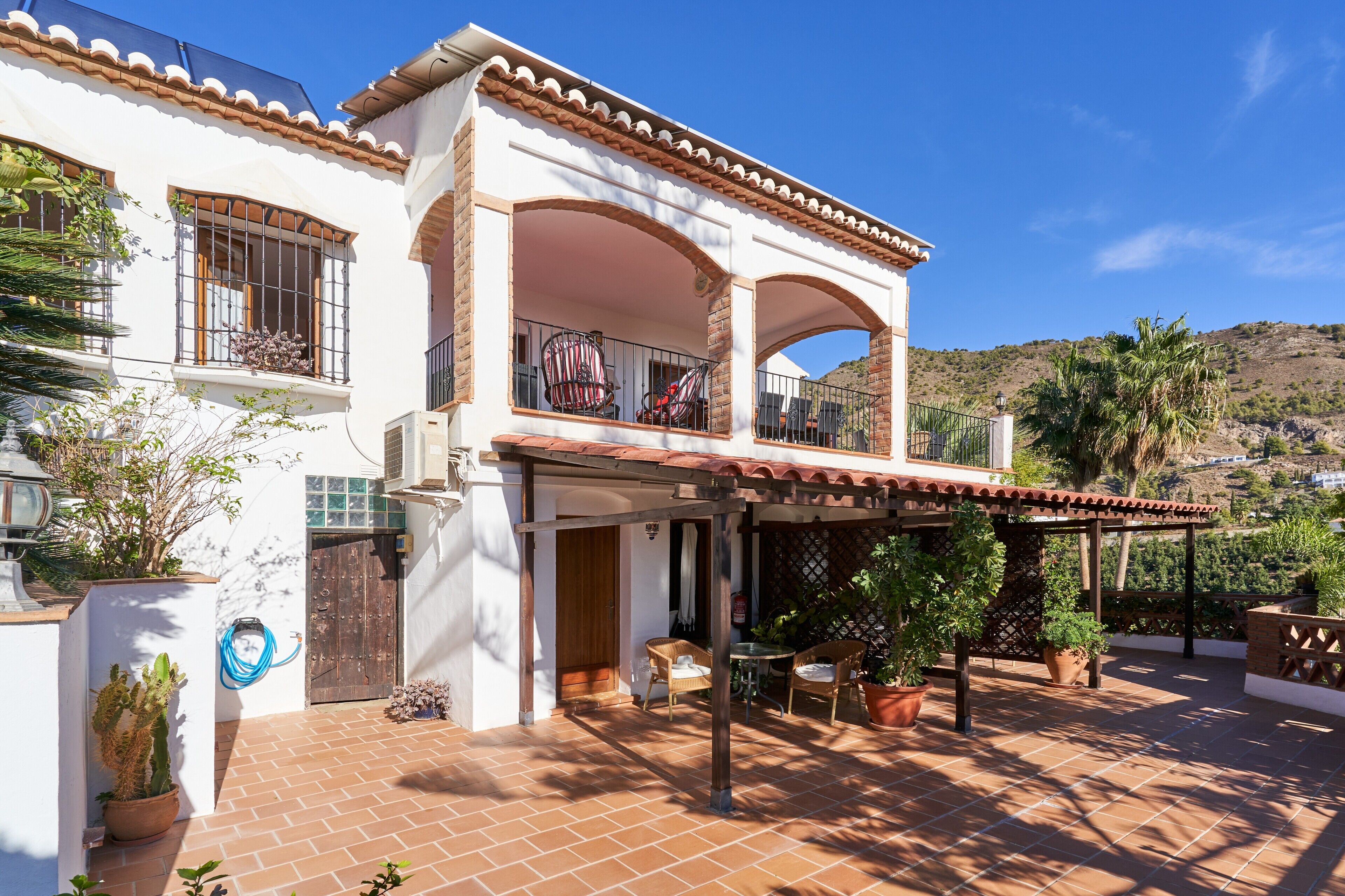 Un edificio bianco con un balcone, piante in vaso e un patio piastrellato.
