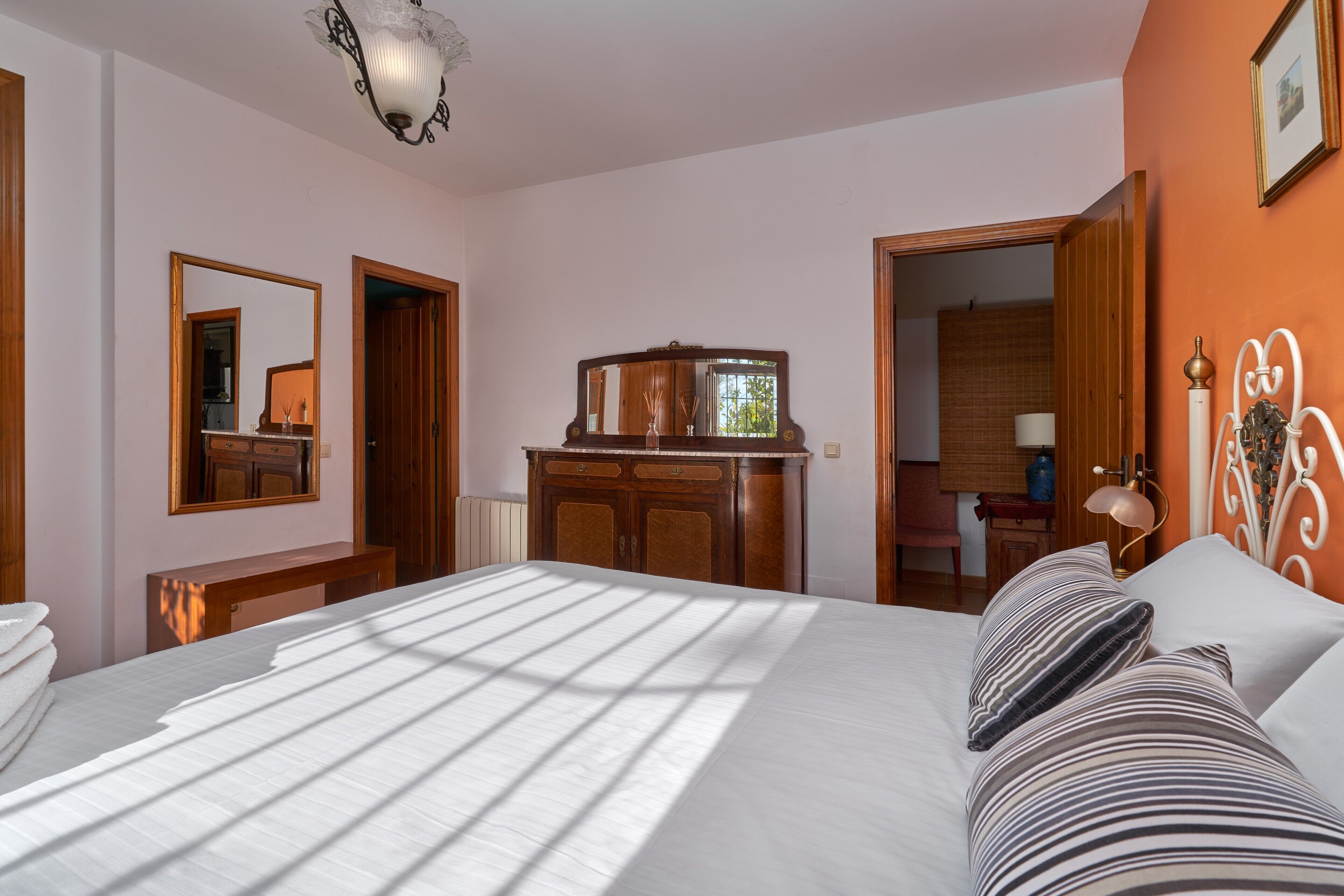 A hotel room with a bed, a dresser, a mirror, and a door leading to another room.