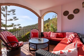 A covered outdoor seating area with a round table, cushioned chairs, and sofas with red and white striped cushions.