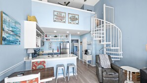 Una cocina moderna con una isla central, electrodomésticos integrados y una escalera en espiral blanca.