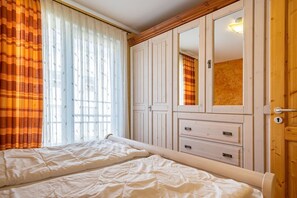 A bedroom with two beds, a wardrobe with multiple drawers, and a mirror.