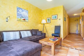 A living room with a sofa, a coffee table, a floor lamp, and a chair. There is a painting on the wall and a vase on the floor.