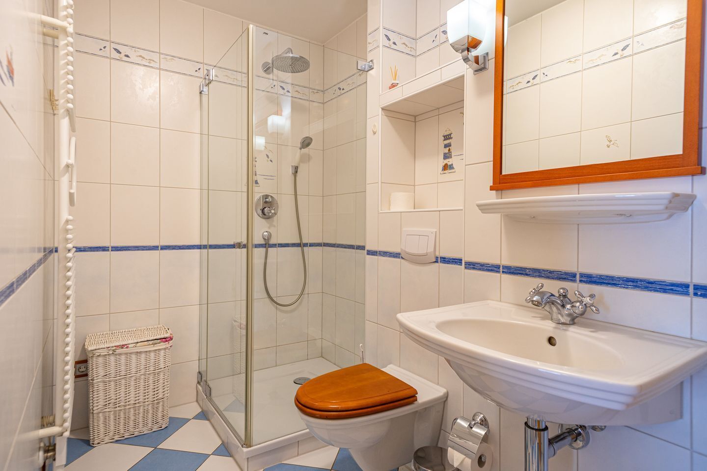Une salle de bain dotée d’une douche à parois de verre, d’un lavabo blanc avec un plan de toilette en bois et de toilettes avec un abattant en bois.