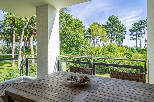 A wooden table with a bowl of stones on a balcony with a metal railing, overlooking a lush green landscape with trees.