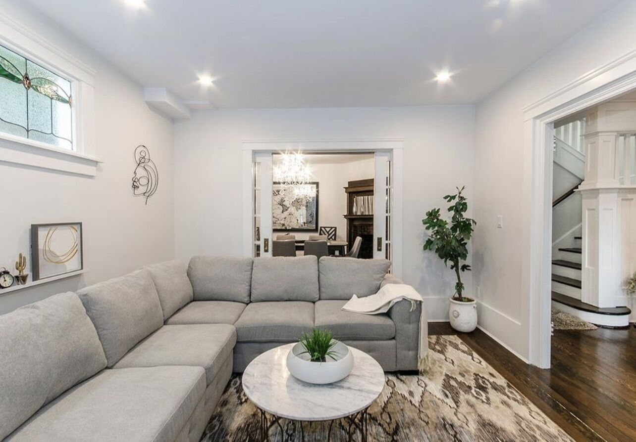 A modern living room with a sectional sofa, a round coffee table with a plant, a patterned rug, and a staircase leading to another level.