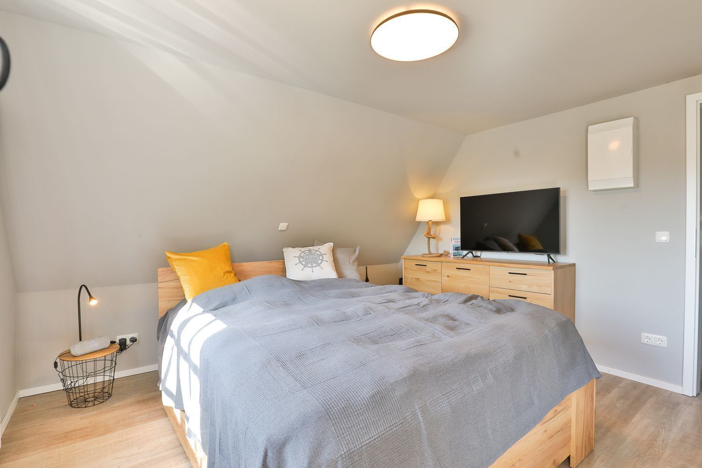 A bedroom with a bed, bedside lamp, TV, and a small table with a lamp.