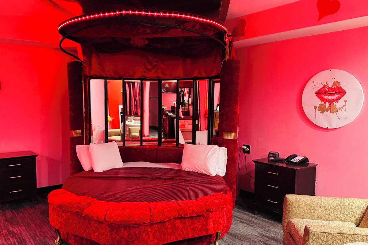Une chambre à coucher aux couleurs rouge, avec un lit à baldaquin, une décoration murale en forme de cœur et une œuvre d’art représentant des lèvres.