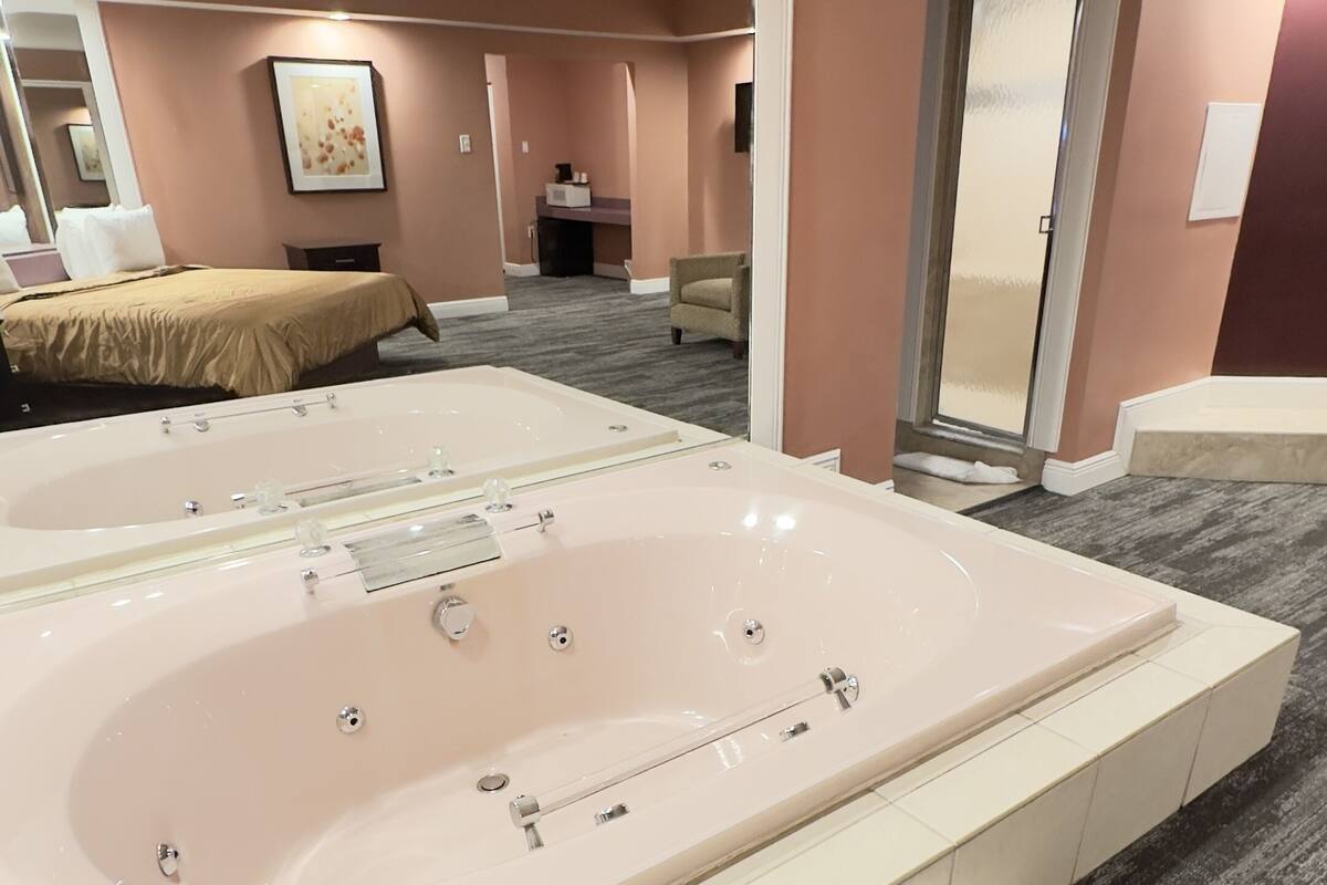 Une grande salle de bain moderne avec une baignoire centrale, un miroir et une porte donnant sur une autre pièce.