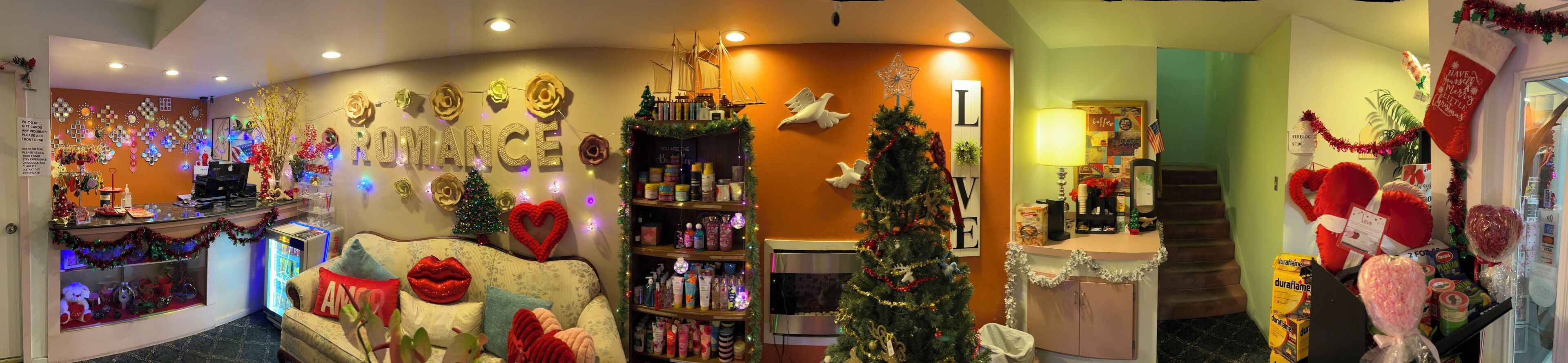 A warmly decorated hotel lobby with a Christmas tree, a heart-shaped decoration, and a variety of gifts and toiletries on shelves.