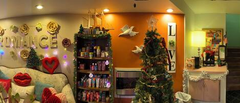 A warmly decorated hotel lobby with a Christmas tree, a heart-shaped decoration, and a variety of gifts and toiletries on shelves.