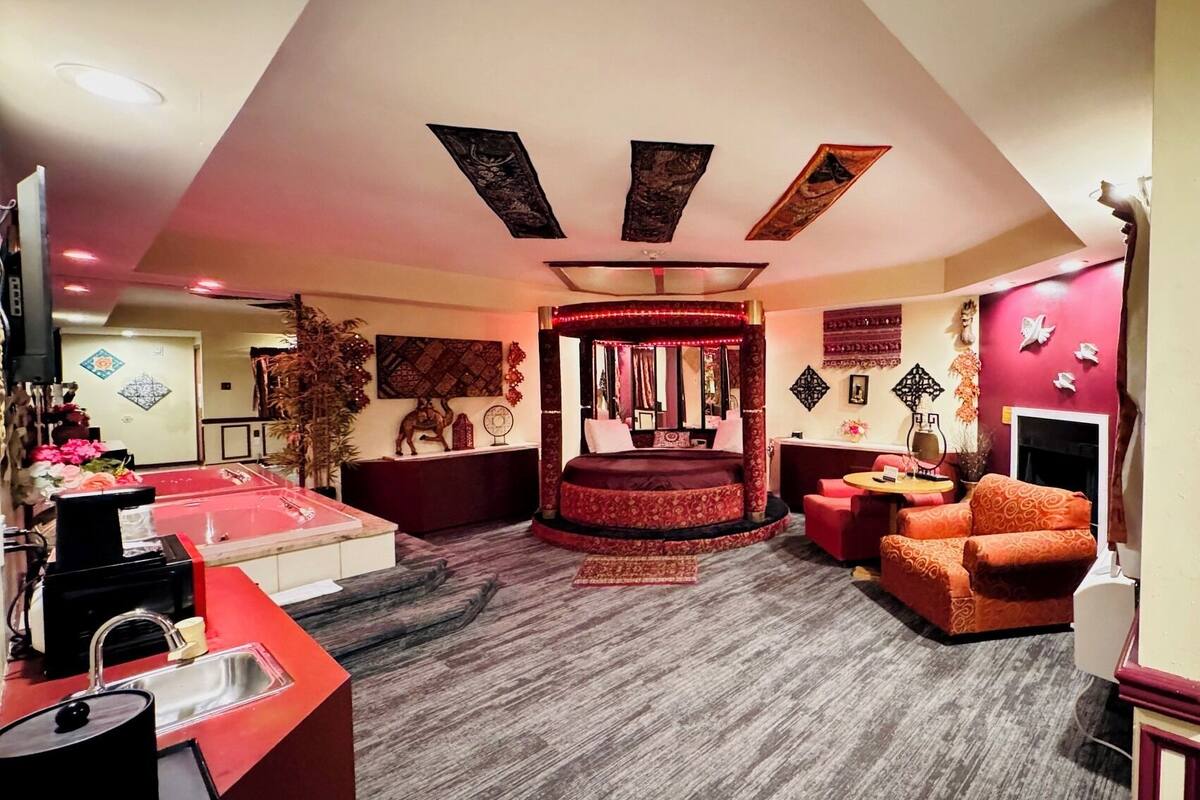 Une chambre avec un lit rond, un coin salon avec un canapé, une cheminée et un petit coin cuisine équipé d’un évier et d’une bouilloire.